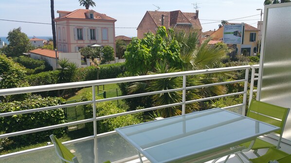 A balcony with a glass table and chairs, overlooking a residential area with houses and greenery.