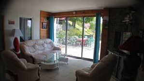 Una sala de estar con un sofá blanco, dos sillones, una mesa de centro de vidrio y una chimenea.