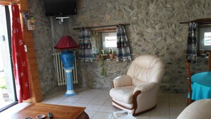 Una habitación con paredes de piedra, un sillón color beige, una mesa de madera y un mantel azul.