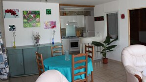 Un comedor con una mesa, sillas y una planta en maceta. Se ve una kitchenette al fondo.
