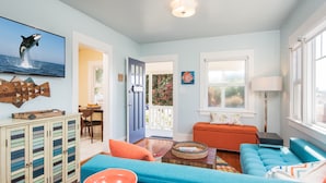 A living room with teal sofas, a wooden cabinet, and a television displaying an orca. - Ocean Beach Sunset Cottage - Steps to Shoreline (San Diego)