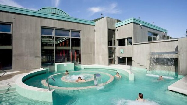 A swimming pool area with multiple water features and a modern building in the background.