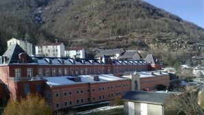 A large red building with multiple windows and a flat roof, surrounded by a hilly landscape.