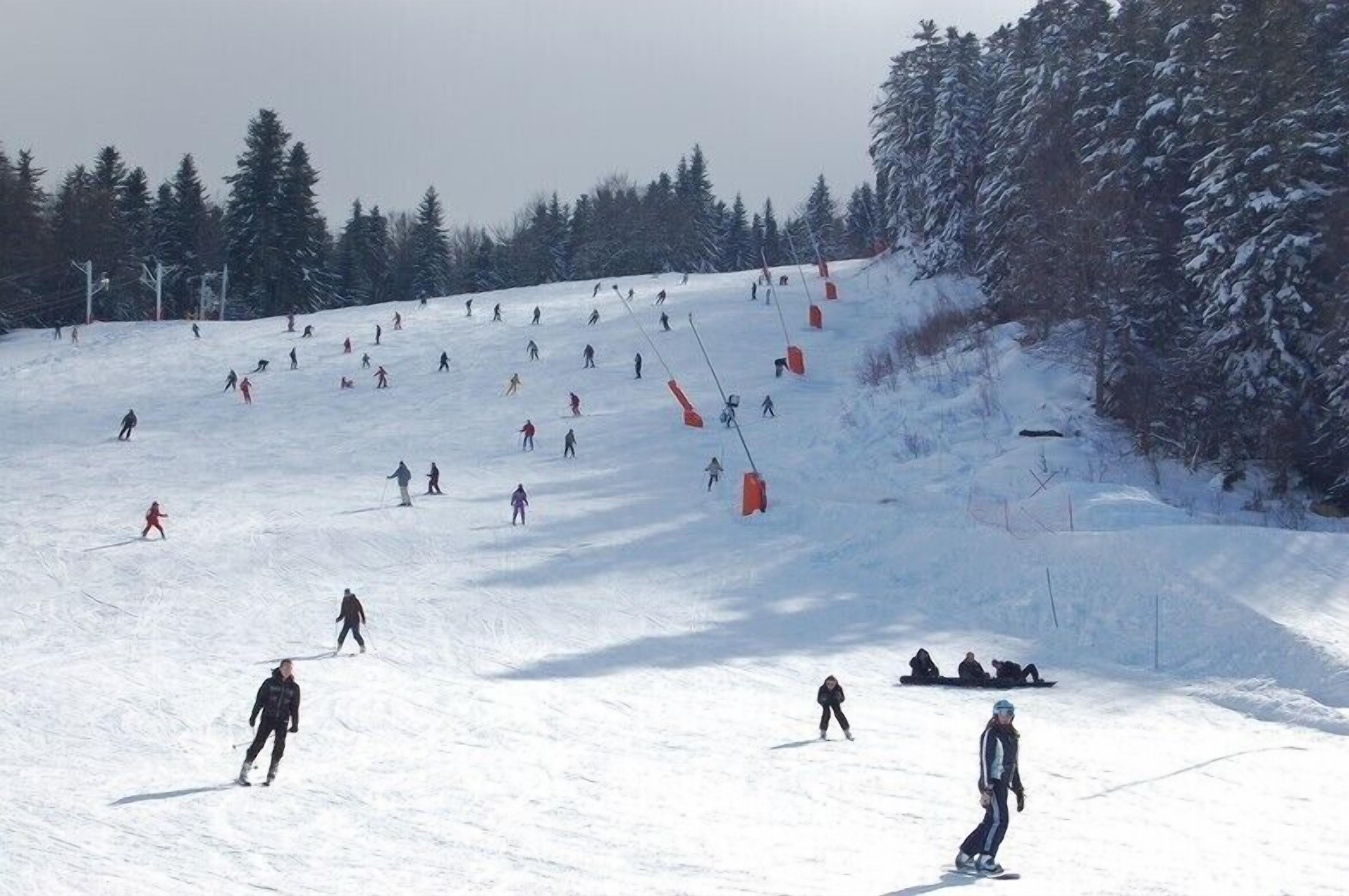 Une piste de ski avec des skieurs et des snowboardeurs, des arbres et un télésiège.