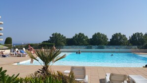 Una piscina con sillones de descanso y vista al mar.