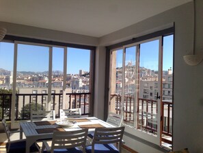 Une pièce avec un balcon, de grandes fenêtres, une table à manger et des chaises.
