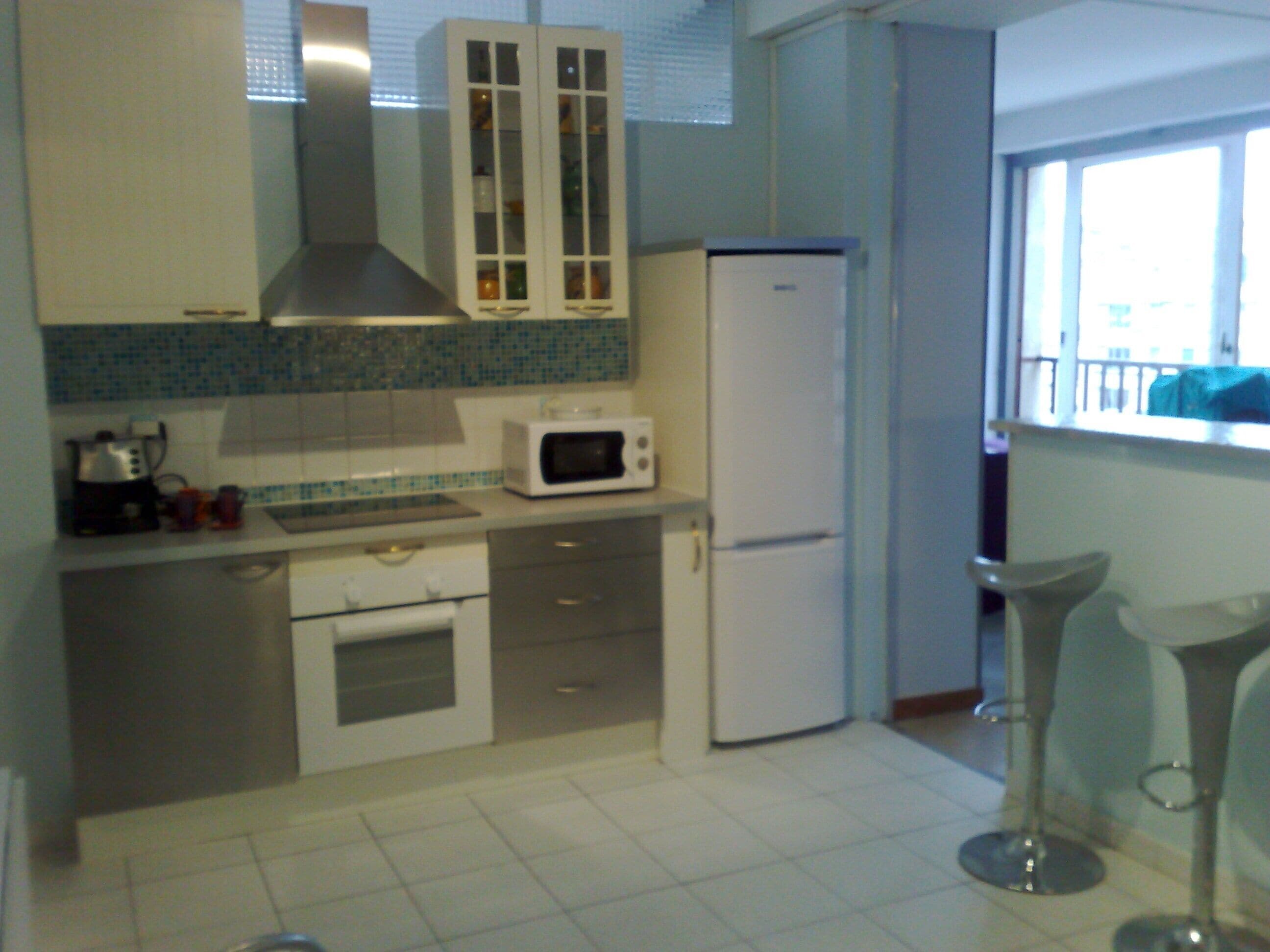 A compact kitchen with white cabinets, a microwave, a refrigerator, and a window with a view.