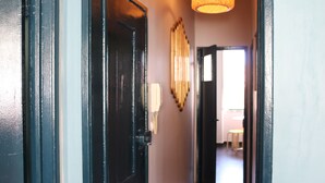 Un pasillo con una puerta negra, un teléfono en la pared y una lámpara colgante.