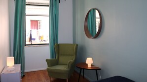 Una habitación con un sillón verde, una mesita con una lámpara y una ventana con cortinas color turquesa.