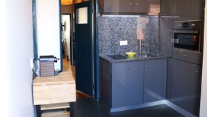 Una cocina moderna con armarios oscuros, encimera de granito y electrodomésticos de acero inoxidable, incluyendo un refrigerador y un horno.