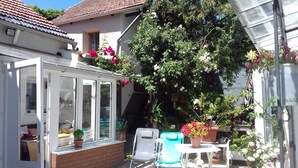 Une véranda avec une porte vitrée, une chaise blanche, une petite table et des plantes en pot.