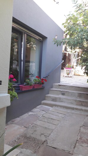 A residential building with a window overlooking a garden. There are steps leading up to the entrance, and a small outdoor area with potted plants. - On the wine road close to Strasbourg (Mutzig)