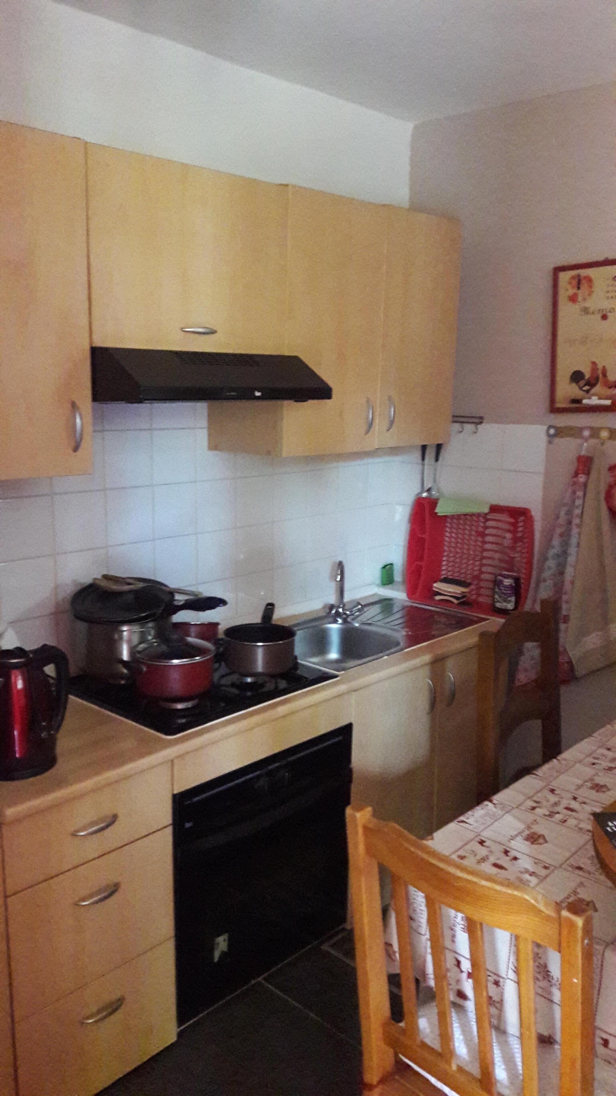 Una cocina compacta con armarios de madera, estufa, lavaplatos y un fregadero.