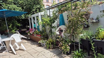 Un patio con plantas en macetas, una silla de plástico blanca y una sombrilla azul.