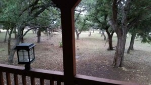 A covered outdoor area with a wooden railing, a lantern, and trees in the background. - BirdHouse Suite @ HomeAway Ranch (Boerne)