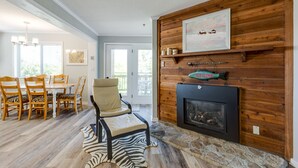 A living room with a fireplace, wooden paneling, a zebra rug, and a dining area with wooden chairs and a table.
