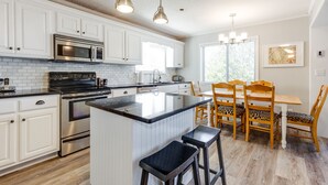 A modern kitchen with white cabinetry, stainless steel appliances, a central island with bar stools, and a dining area with wooden chairs and a table.