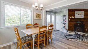 A dining area with a wooden table and chairs, a chandelier, and a fireplace.