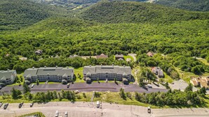 An aerial view of a campus with multiple buildings, parking areas, and surrounding forested hills.