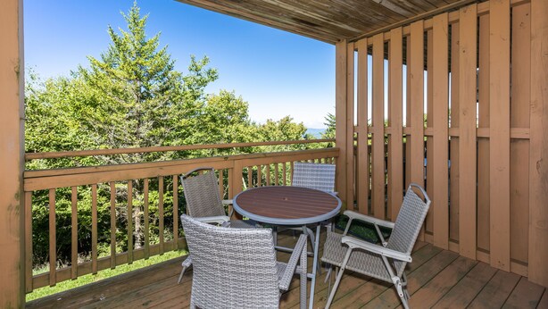 A covered outdoor area with a wooden deck, a round table, and four wicker chairs.