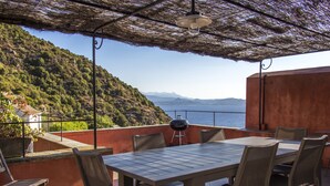 Une terrasse extérieure avec une table et des chaises, un barbecue et une vue sur la mer et les collines.