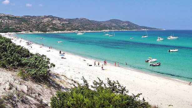 Une plage avec une eau turquoise et limpide, des bateaux et des gens.