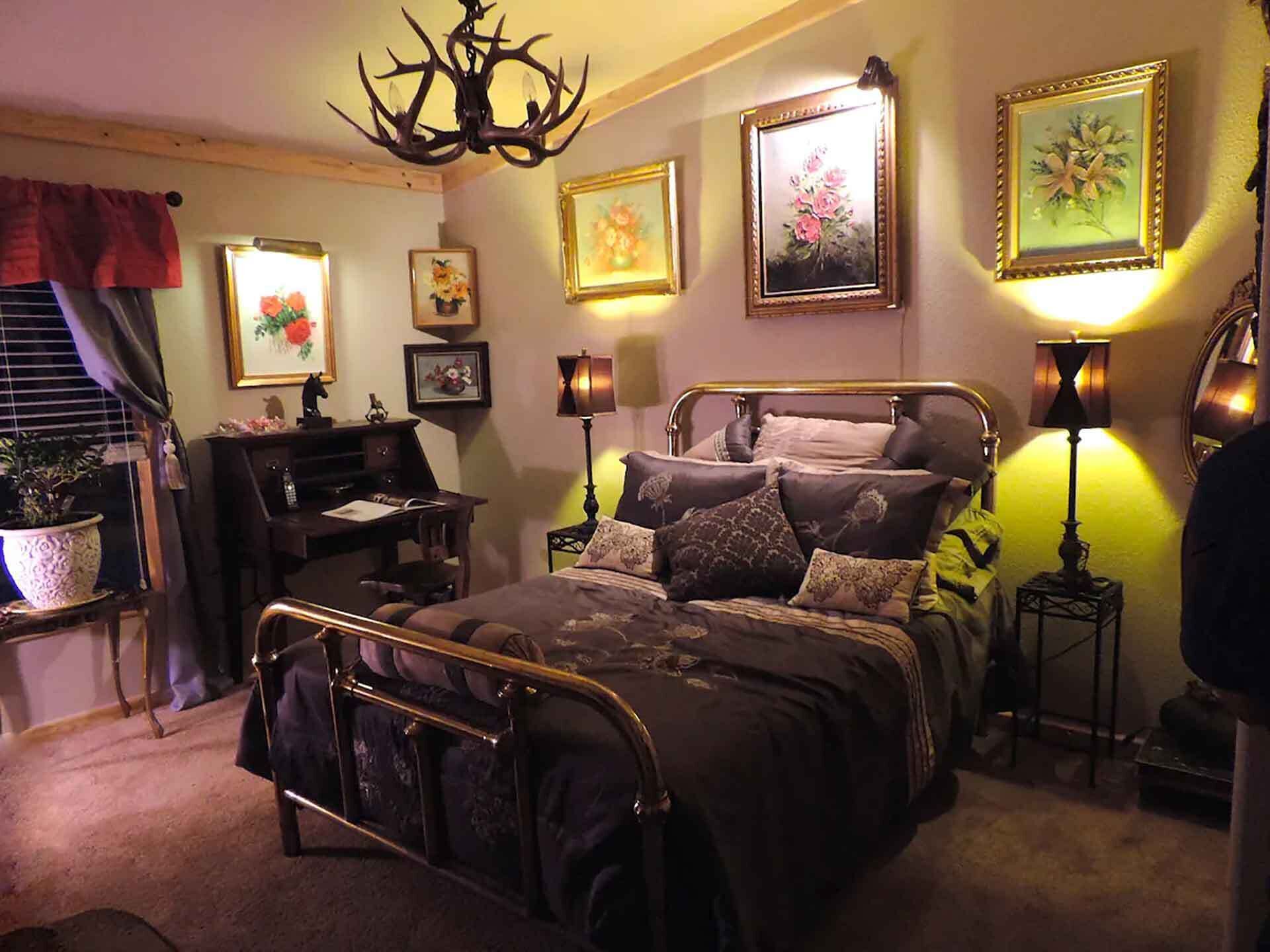 A bedroom with a four-poster bed, a desk, and a chair. There are two lamps on either side of the bed.