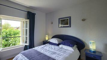Un dormitorio con una cama, una mesita de noche con lámpara, una ventana con cortinas y un cuadro en la pared.