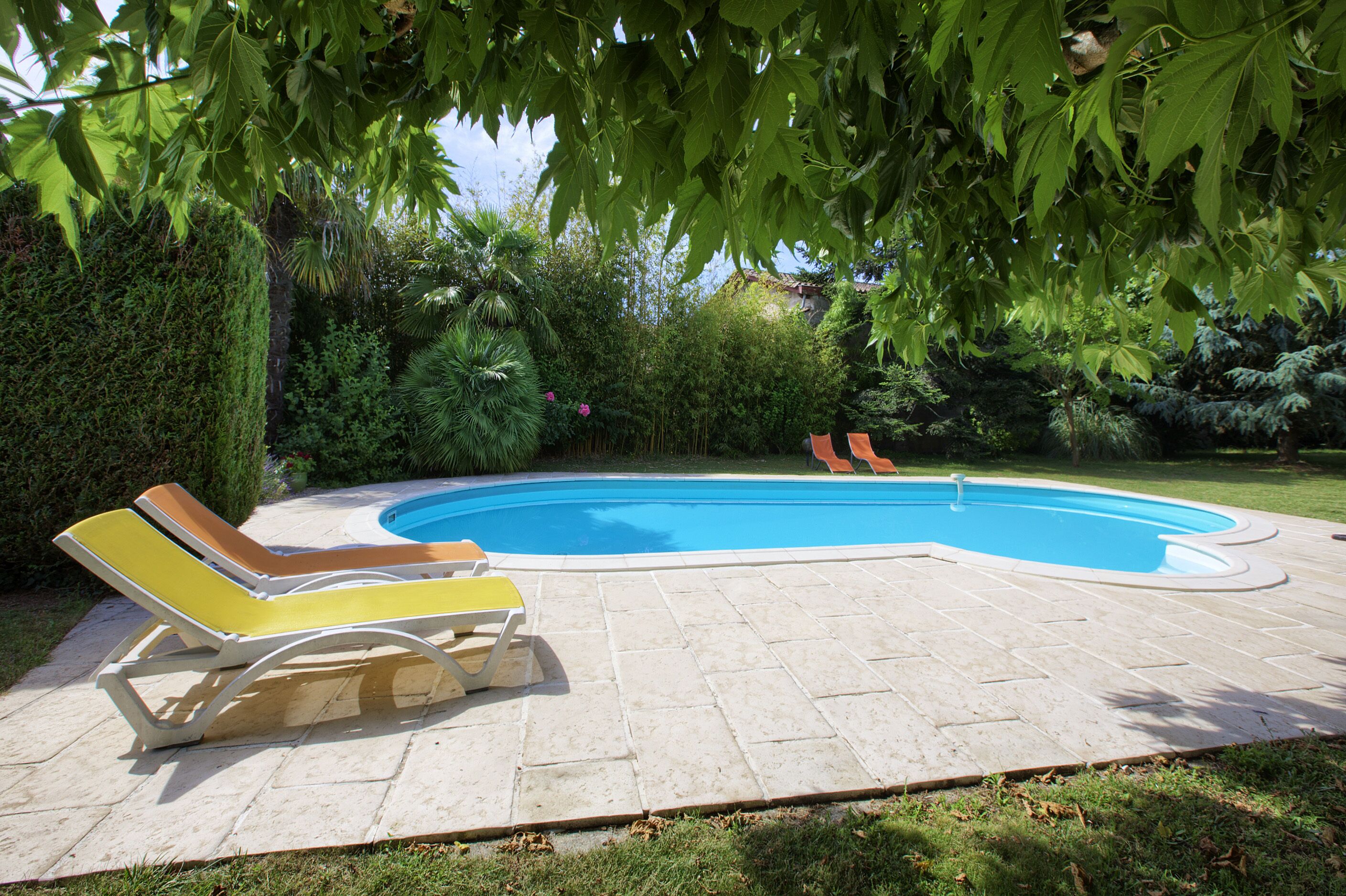 Ein Schwimmbecken mit zwei Liegestühlen und einer gefliesten Liegefläche.
