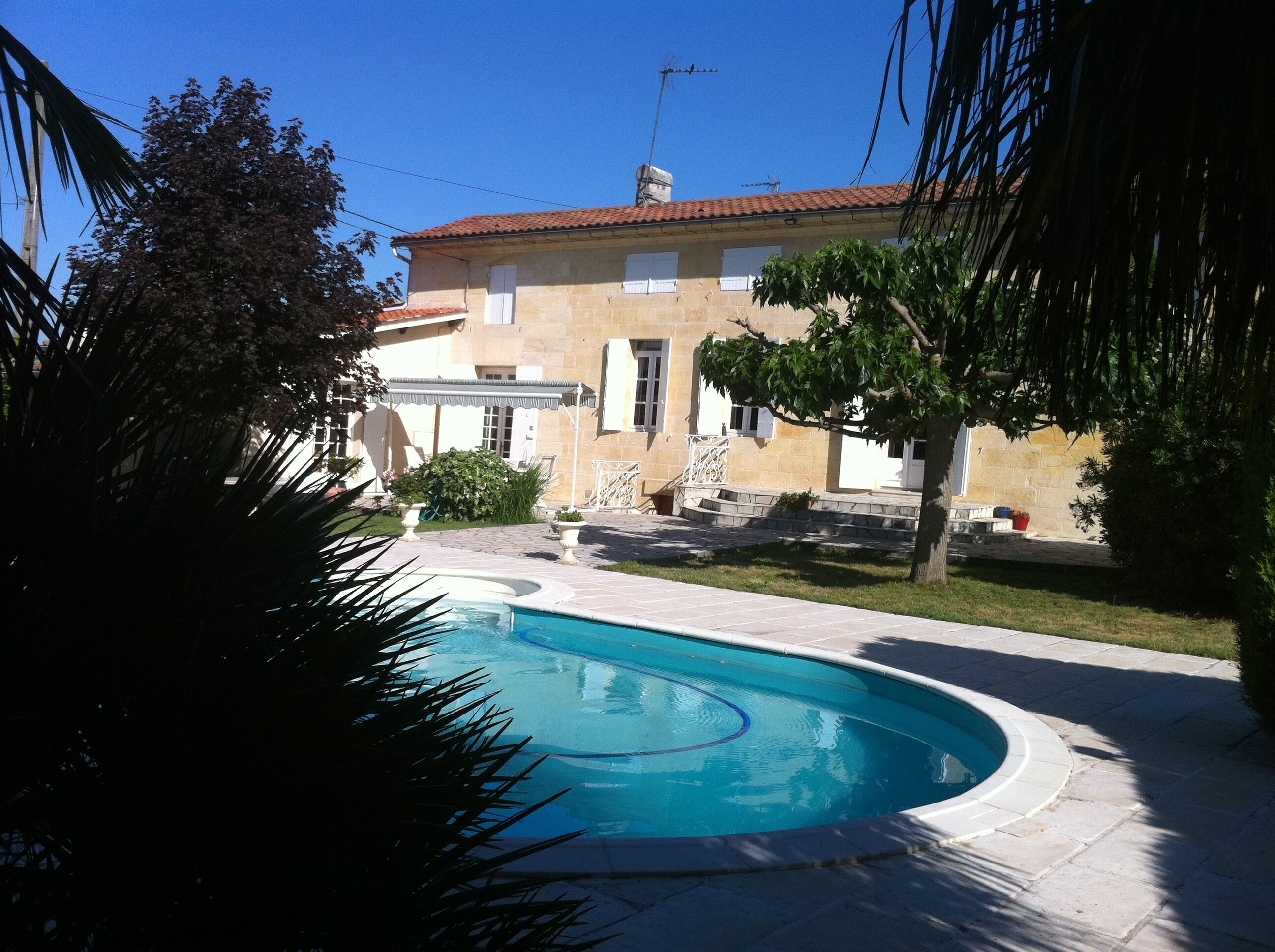 A swimming pool with a stone deck, a stone building with a tiled roof, and a well-maintained lawn.