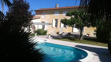 A swimming pool with a stone deck, a stone building with a tiled roof, and a well-maintained lawn.