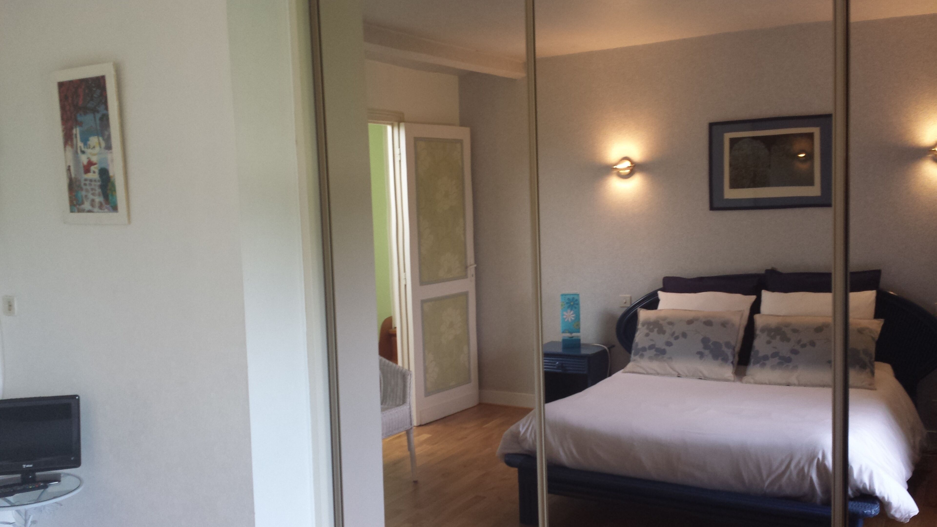 A bedroom with a bed, bedside tables, a TV, and a door leading to another room.