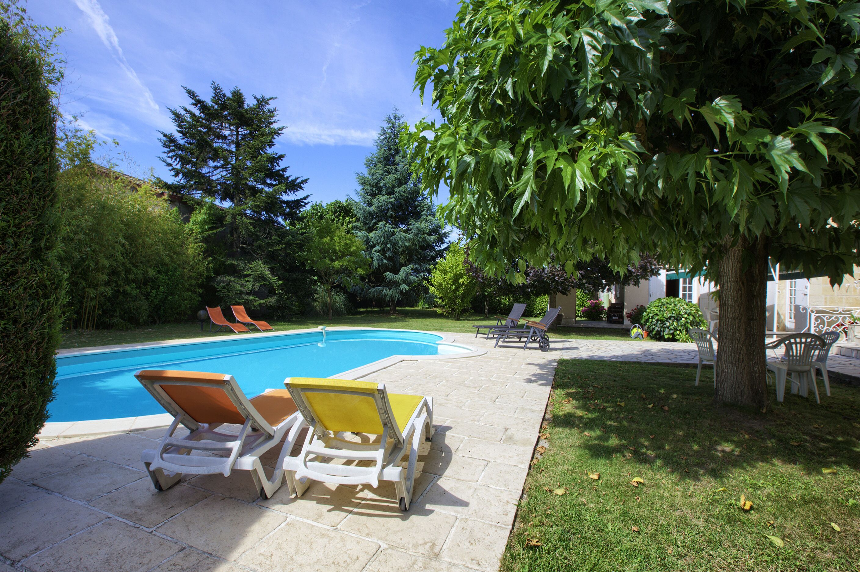 Une piscine avec des chaises longues et un arbre dans un jardin.