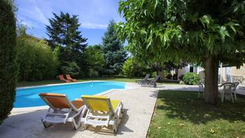 Une piscine avec des chaises longues et un arbre dans un jardin.