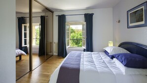 Ein Schlafzimmer mit Bett, einem Fenster mit Vorhängen, einem Heizkörper und einer Tür zu einem anderen Raum.