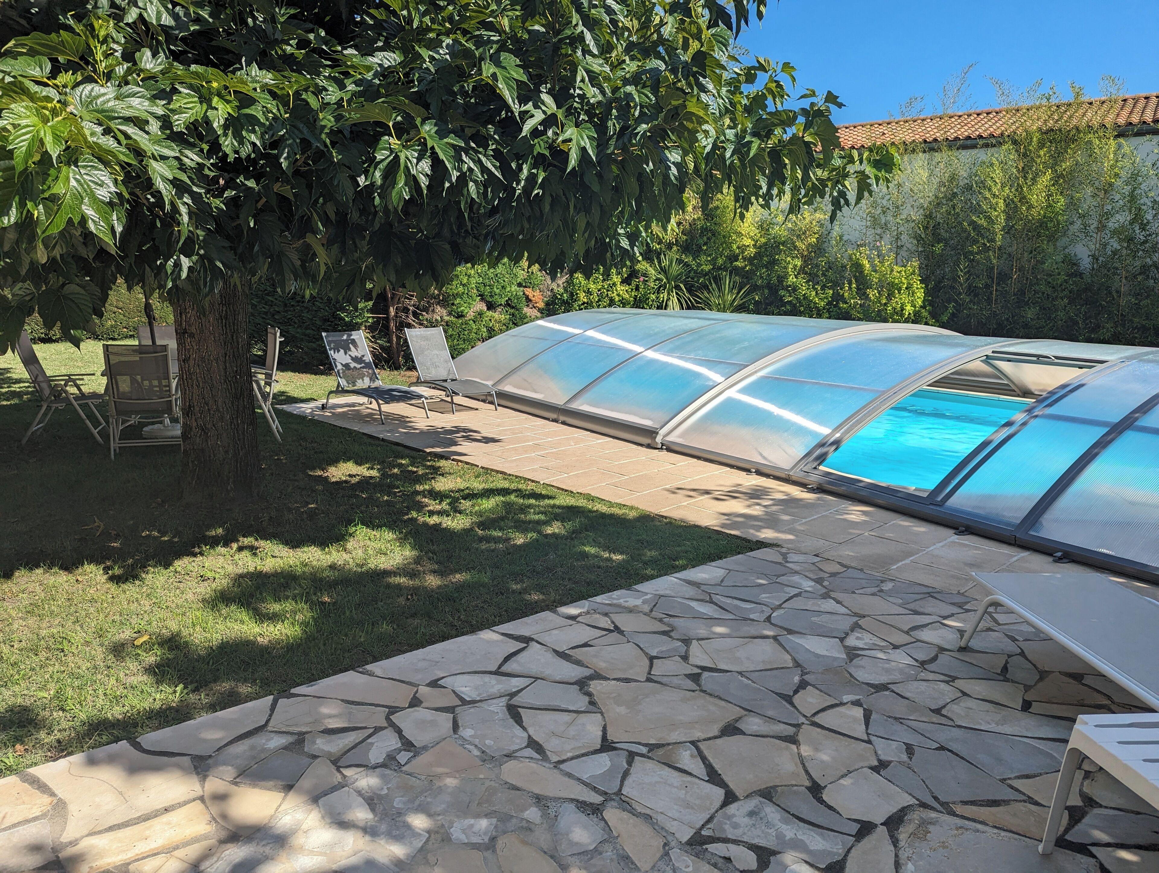 Una estructura de invernadero con piscina, patio de piedra y zona de estar exterior.