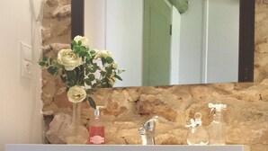 A bathroom vanity with a stone wall backdrop, a mirror, and a vase of flowers. - French Holiday rental in the Périgord. XVIII th Century stone farmhouse. (Villefranche-Du-Périgord)
