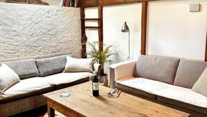 A cozy living room with a wooden coffee table, two sofas, a stone accent wall, and a skylight. - French Holiday rental in the Périgord. XVIII th Century stone farmhouse. (Villefranche-Du-Périgord)