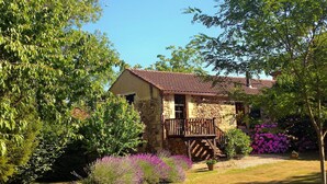 A stone house with a wooden balcony, surrounded by lush greenery and flowering plants. - French Holiday rental in the Périgord. XVIII th Century stone farmhouse. (Villefranche-Du-Périgord)