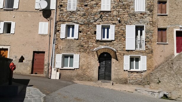 Un edificio de piedra con múltiples ventanas, algunas con contraventanas, y una puerta central.