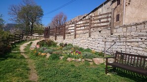 Un muro de piedra con una valla de madera, un banco y un jardín con diversas plantas y flores.