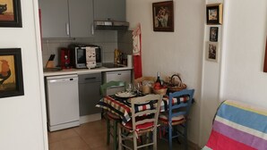 Cocina compacta equipada con microondas, tostadora y refrigerador pequeño. Se observa una mesa de comedor con sillas y mantel colorido.