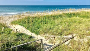 Een strand met een houten vogel kijken looppad dat naar de kust leidt, omringd door duinen en grasrijke begroeiing.