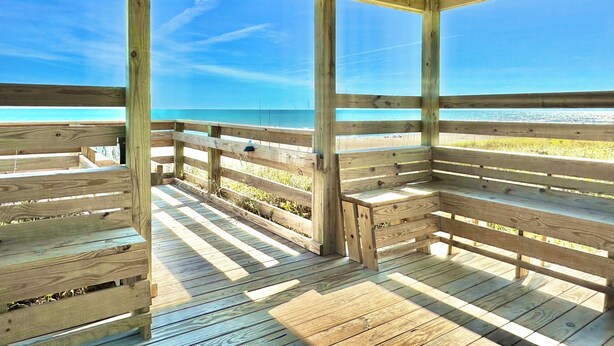 Een houten terras met banken, met uitzicht op een strand.