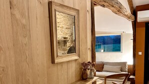 A rustic interior with exposed wooden beams, a stone wall, a framed picture, and a wooden shelf with a vase. - The small sheepfold in the Perigord (Villefranche-Du-Périgord)