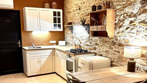 A kitchen with a stone wall, wooden cabinets, a stove, and a dining table with chairs. - The small sheepfold in the Perigord (Villefranche-Du-Périgord)