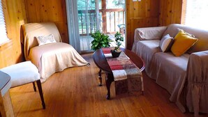 A cozy cabin interior with a bed, a sofa, a small table, and a window with a view of trees. - Butterflies Cabin @ HomeAway Ranch (Boerne)