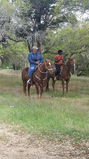Deux personnes à cheval dans un espace herbeux, avec des arbres en arrière-plan.
