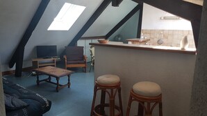 A cozy attic room with a sloped ceiling, a television, a wooden table, two bar stools, and a small kitchen area with a sink and a window. - Studio near the marina of Vannes, for 4 people  (Vannes)