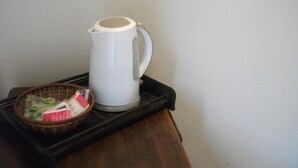 Een witte waterkoker op een zwart dienblad, met een mandje met een theezakje en een klein voorwerp.